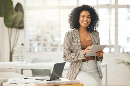 Happy businesswoman using a digital tablet. Young leading businesswoman using a wireless tablet. Creative designer working in her agency. Designer standing in her office using an online app.