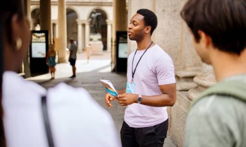 A group of multiracial people have a tour guide as they explore the city of Milan